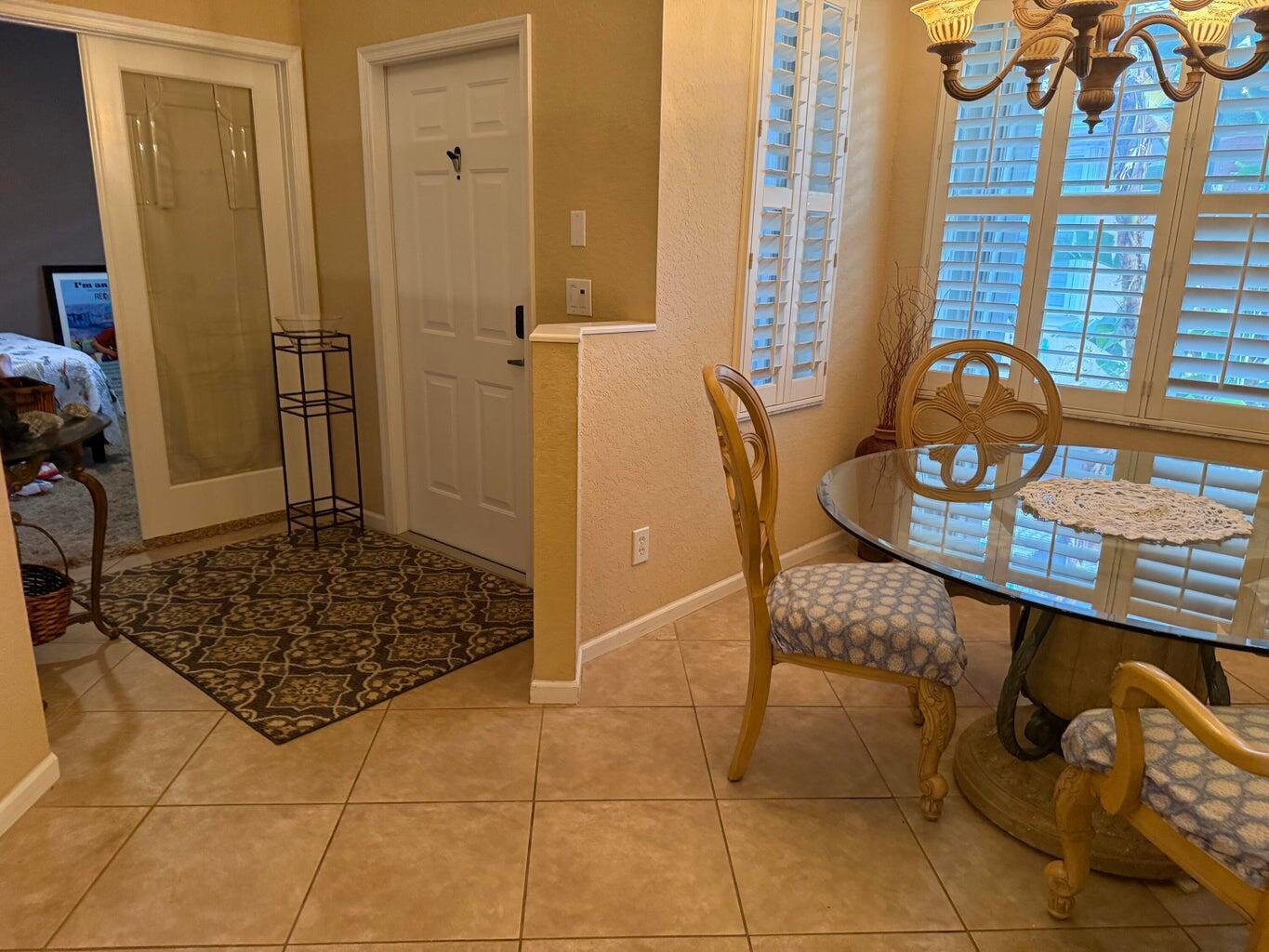 A dining area with a glass table, patterned chairs, and a tile floor near an entryway — 328 W Coral Trace Circle, Delray Beach FL 33445, DELRAY BEACH, FL