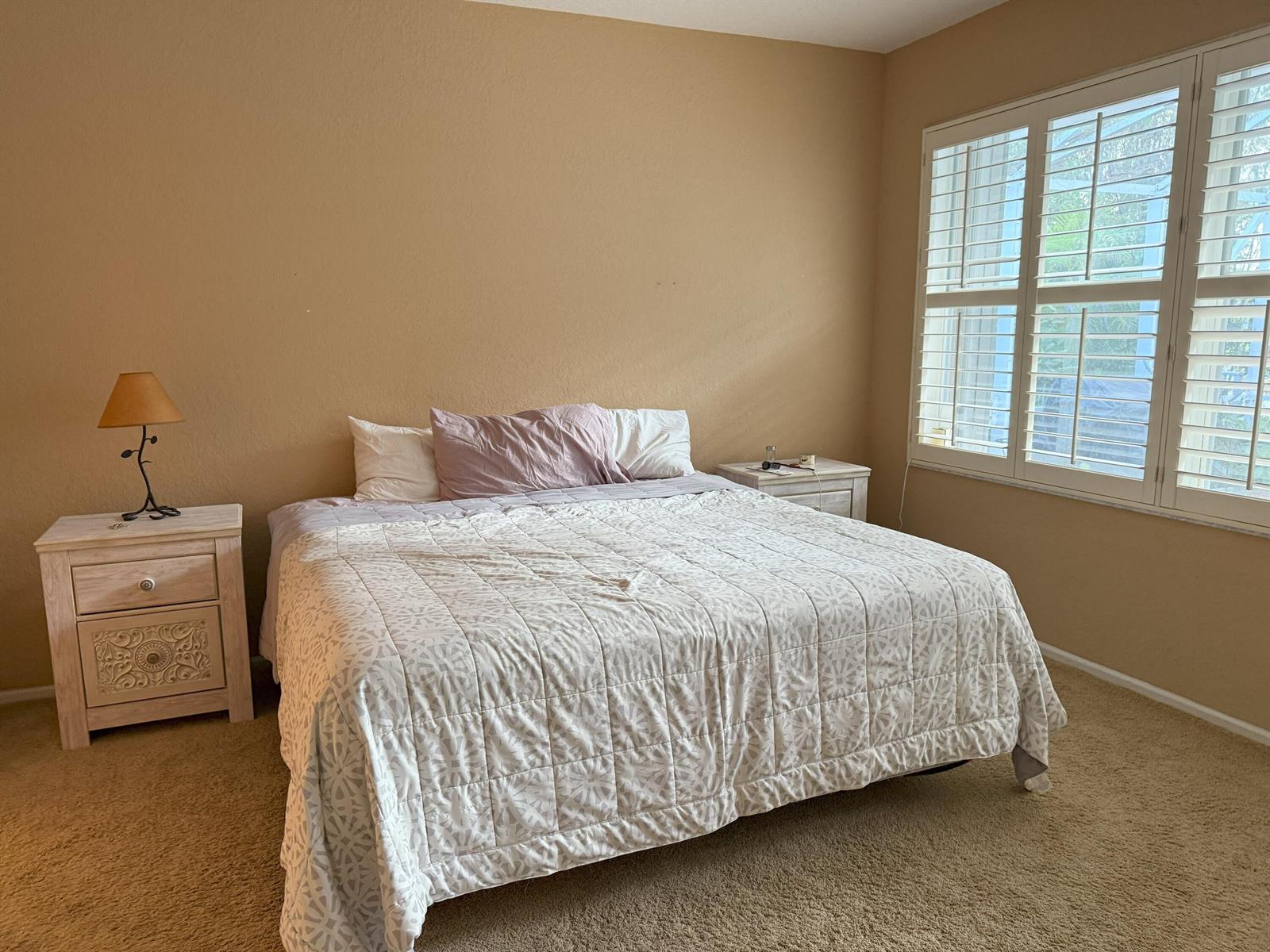 A bedroom features tan walls, beige carpeting, a bed with a patterned quilt, and plantation shutters — 328 W Coral Trace Circle, Delray Beach FL 33445, DELRAY BEACH, FL