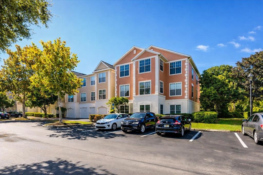 A three-story apartment building with a parking lot in front under a clear blue sky — 12849 MADISON POINTE CIRCLE UNIT 307, ORLANDO, FL