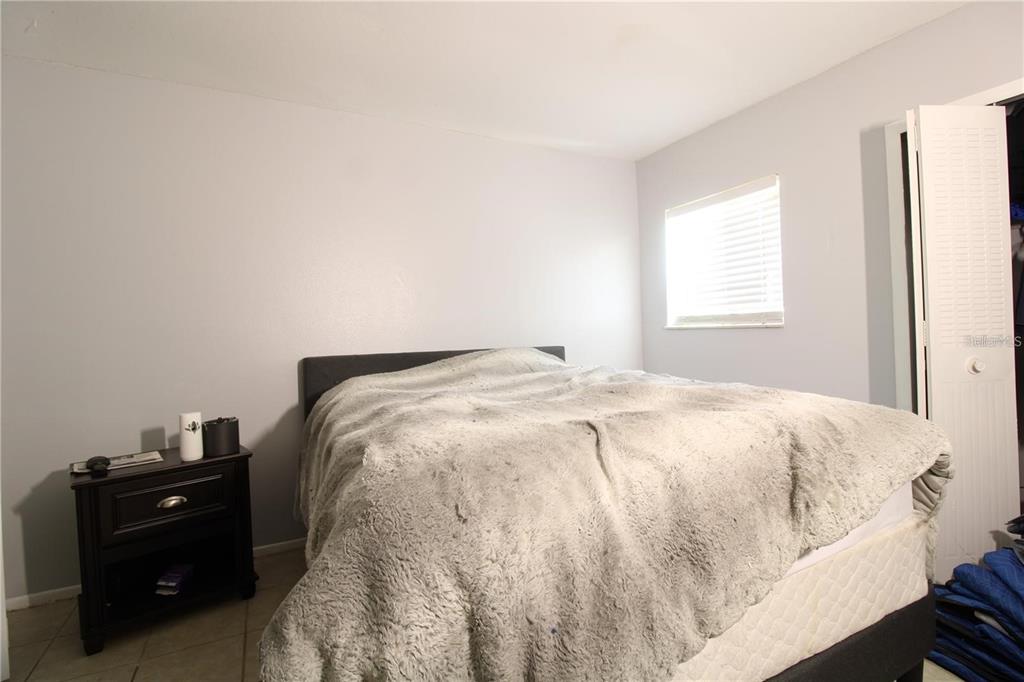 A bedroom features a bed with a gray fuzzy blanket, a nightstand, and a window — 311 SCOTTSDALE SQUARE UNIT 311, WINTER PARK, FL