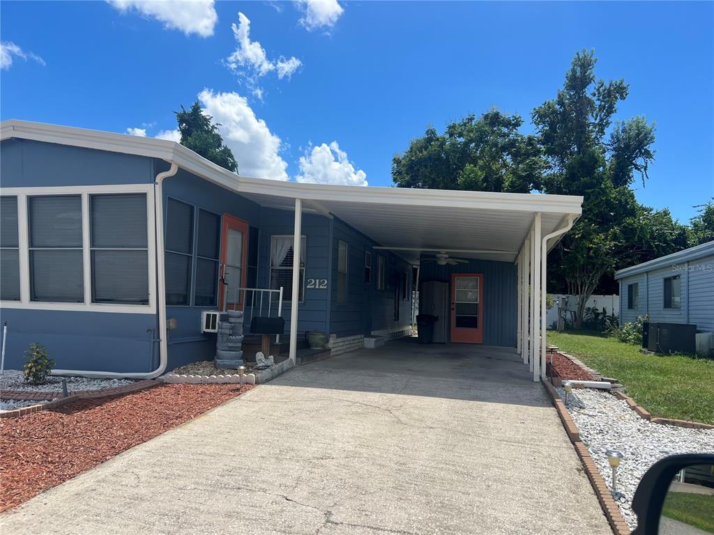 A blue manufactured home features a concrete driveway, a covered carport, and orange doors — 212 PARADISE S, LEESBURG, FL