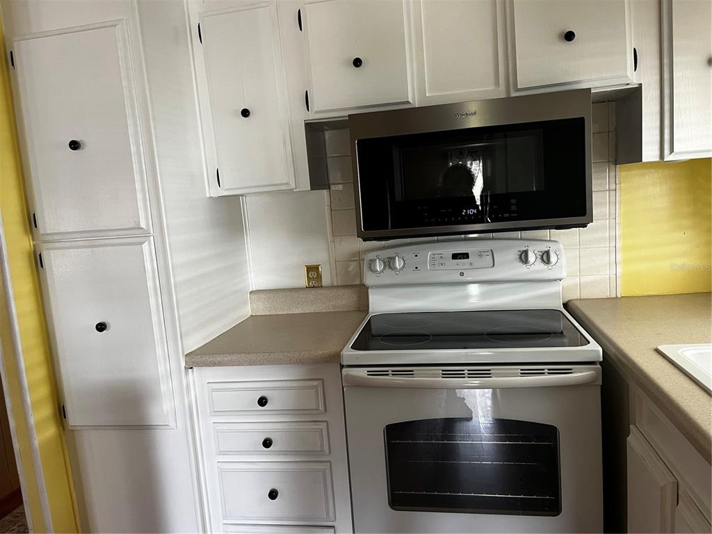 A kitchen features white cabinets, a white electric range, and a stainless steel microwave — 212 PARADISE S, LEESBURG, FL
