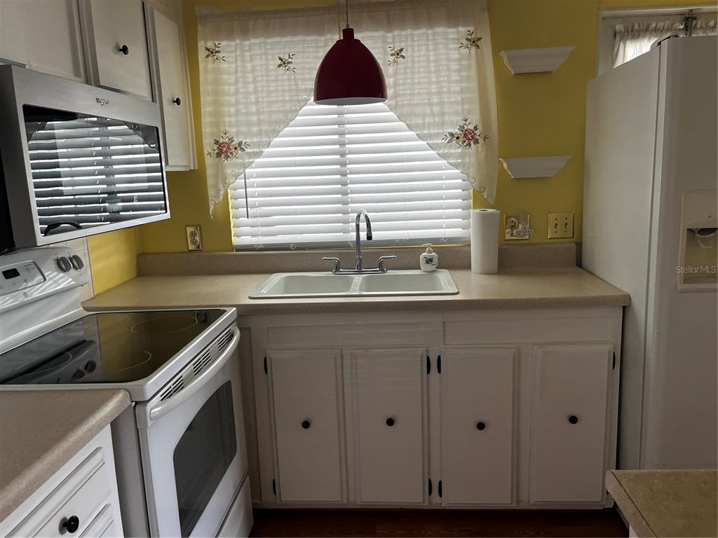 A kitchen features white cabinets, a double-basin sink, a white stove, and yellow walls — 212 PARADISE S, LEESBURG, FL