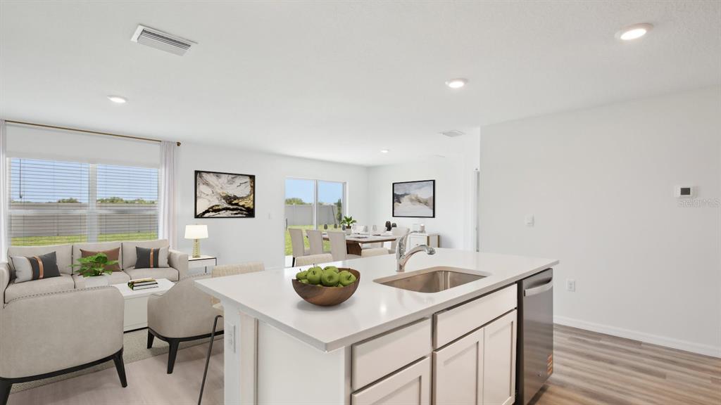 A kitchen island with a sink overlooks an open-concept living and dining area — 12435 HOPSCOTCH AVENUE, PARRISH, FL