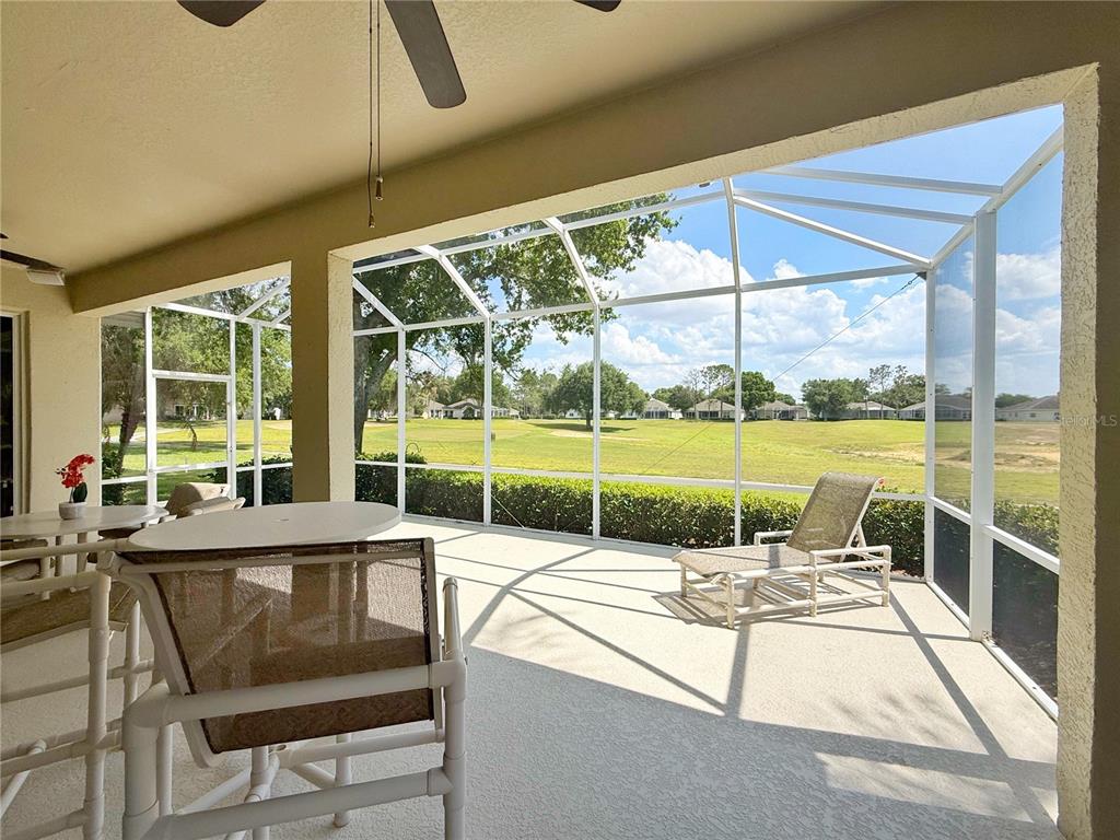 A screened-in patio overlooks a grassy golf course with a lounge chair and table — 3445 CAPLAND AVENUE, CLERMONT, FL