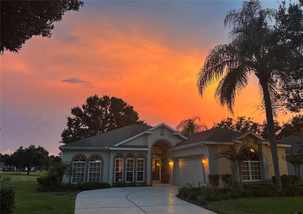 A single-story house with a concrete driveway and palm tree under a vibrant sunset sky — 3445 CAPLAND AVENUE, CLERMONT, FL