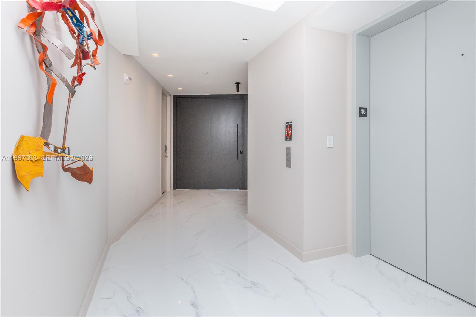 A hallway features white marble flooring, a dark entrance door, and a modern wall sculpture — 851 NE 1st Ave # 4611, Miami FL 33132, MIAMI, FL