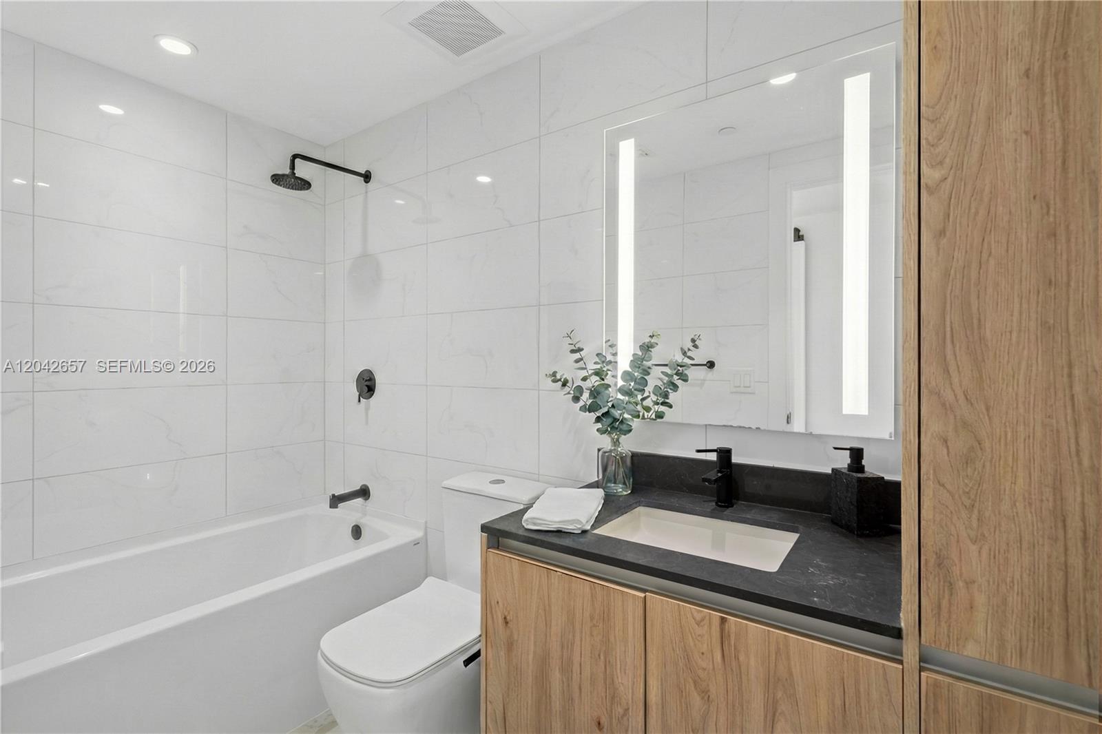 A modern bathroom features a white soaking tub, wood vanity, and black hardware — 650 NE 2nd Ave # 3412, Miami FL 33132, MIAMI, FL