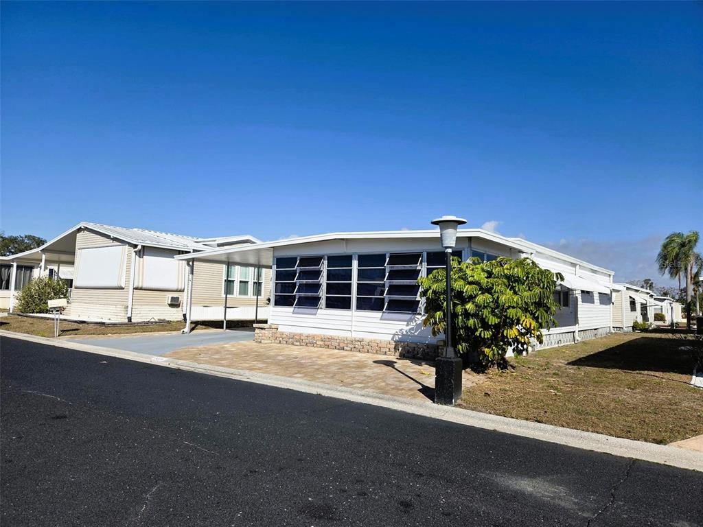 A white manufactured home with a paved driveway and a carport under a blue sky — 3225 SWEET GUM TERRACE, SARASOTA, FL