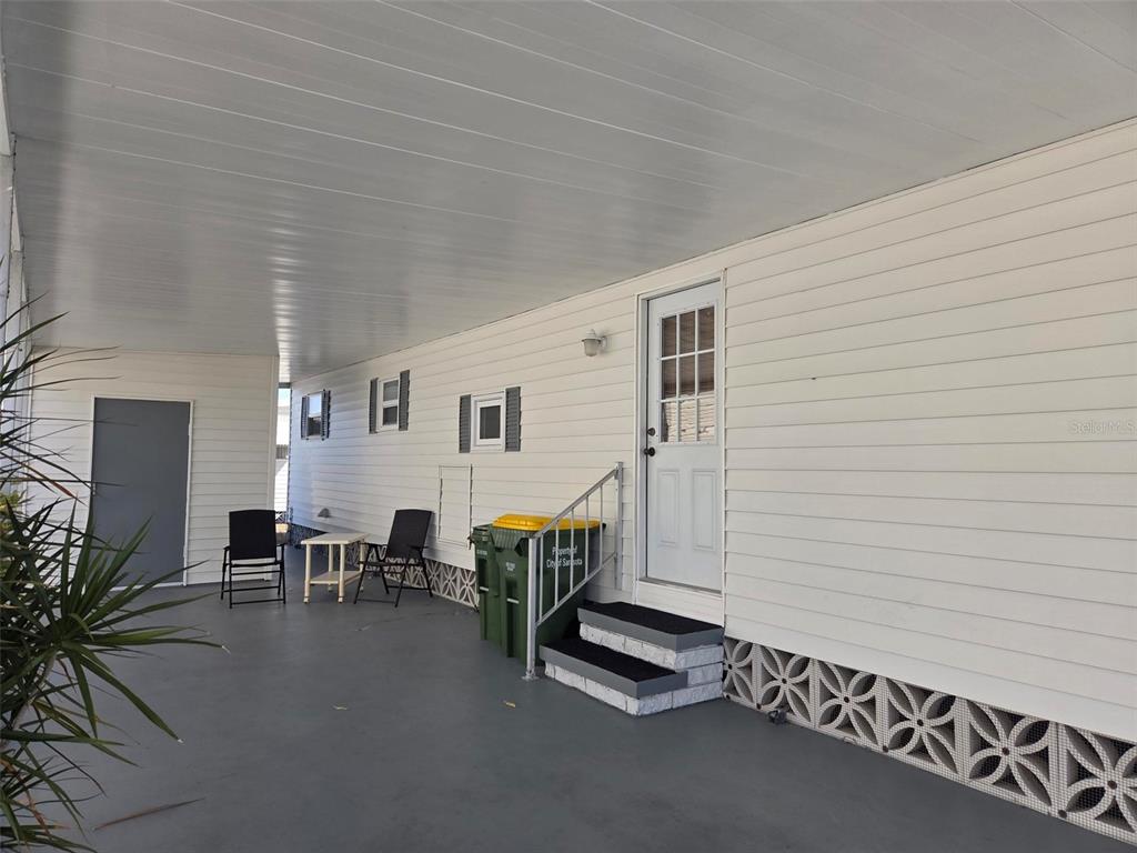 A covered carport area features a white exterior wall, a side door, and concrete steps — 3225 SWEET GUM TERRACE, SARASOTA, FL