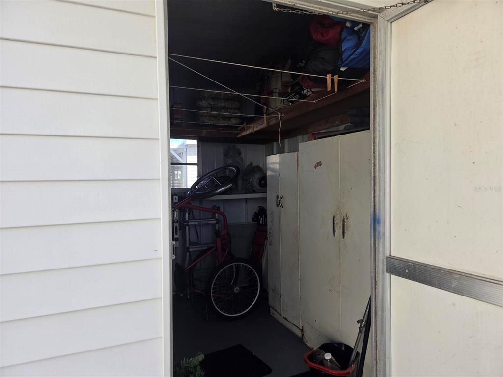 An open door reveals a cluttered storage shed with shelving and a bicycle inside — 3225 SWEET GUM TERRACE, SARASOTA, FL