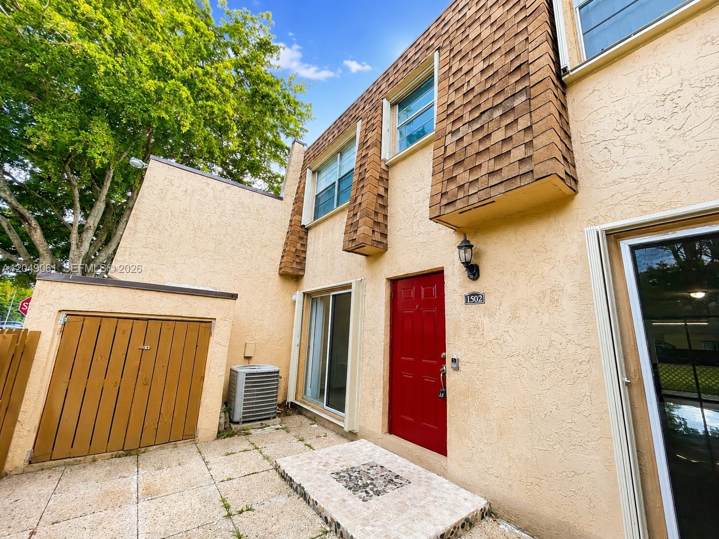 A red front door stands beside a sliding glass door on a stucco townhouse exterior — 3741 NW 95th Ter # 1502, Sunrise FL 33351, SUNRISE, FL