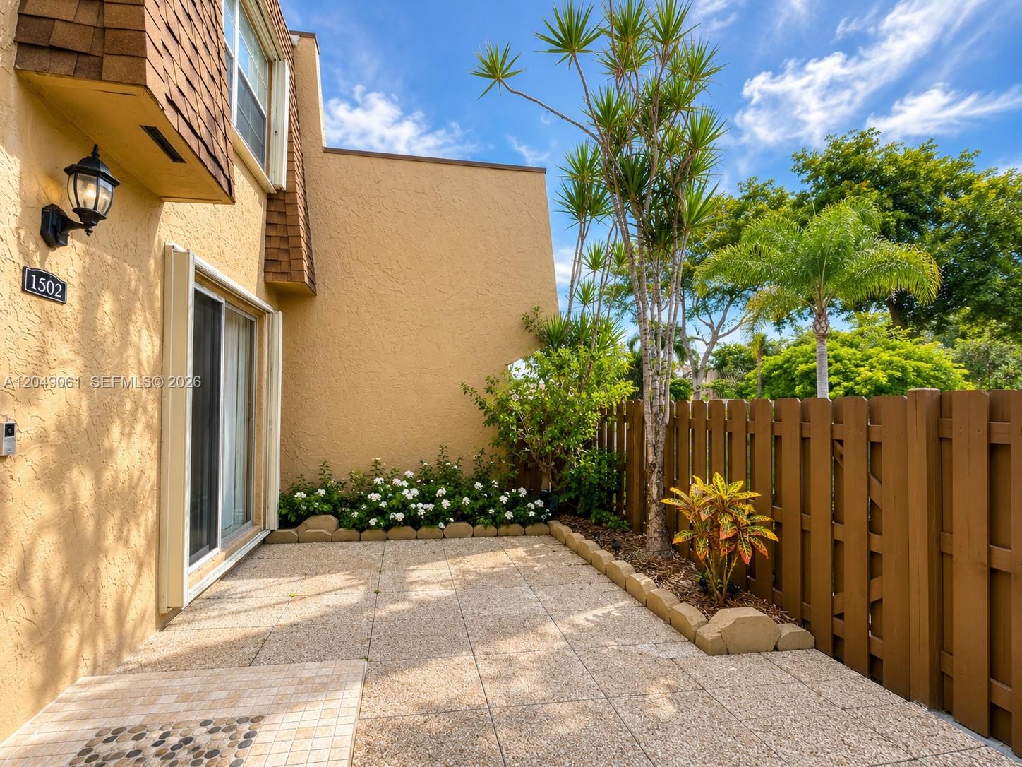 A paved patio area features a small garden bed, a wooden fence, and exterior lighting — 3741 NW 95th Ter # 1502, Sunrise FL 33351, SUNRISE, FL