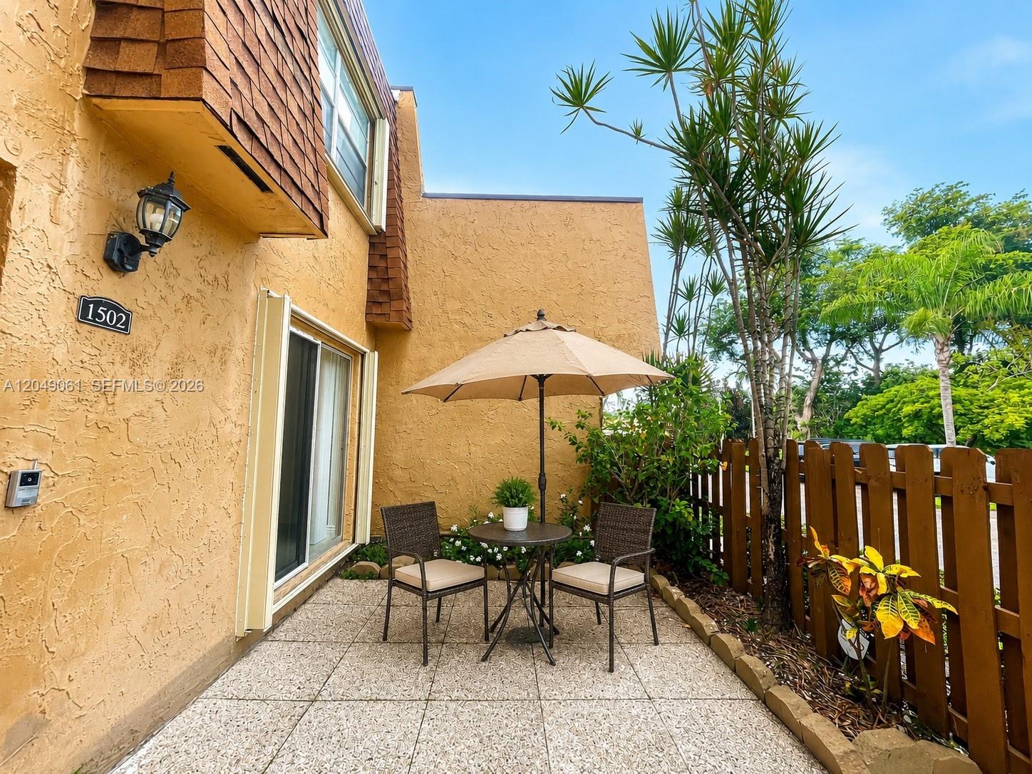 A patio with a table, two chairs, and an umbrella sits beside a stucco building — 3741 NW 95th Ter # 1502, Sunrise FL 33351, SUNRISE, FL