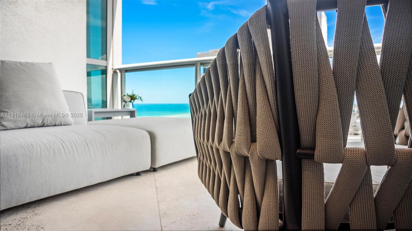 A close-up of a woven outdoor chair on a balcony overlooking the ocean — 101 20th St # 2102, Miami Beach FL 33139, MIAMI BEACH, FL