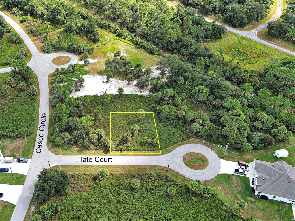 An aerial view shows a vacant, rectangular lot outlined in yellow at a street intersection — TATE COURT, NORTH PORT, FL