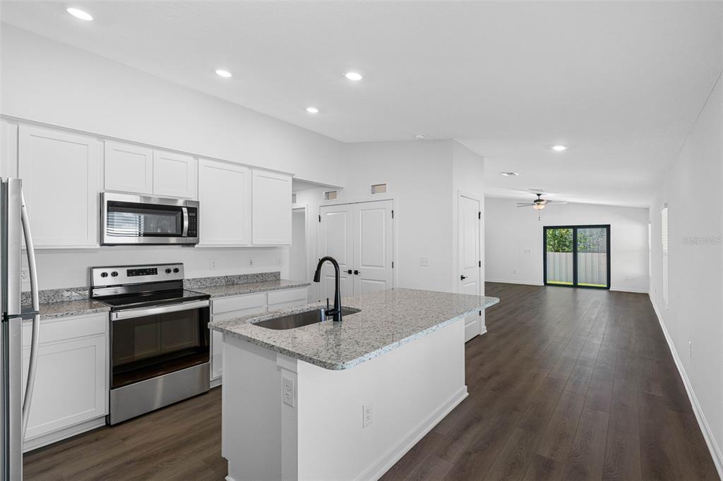A kitchen with white cabinets, granite countertops, and a center island opens to a living area — 573 BLACKTHORN DRIVE, LAKELAND, FL