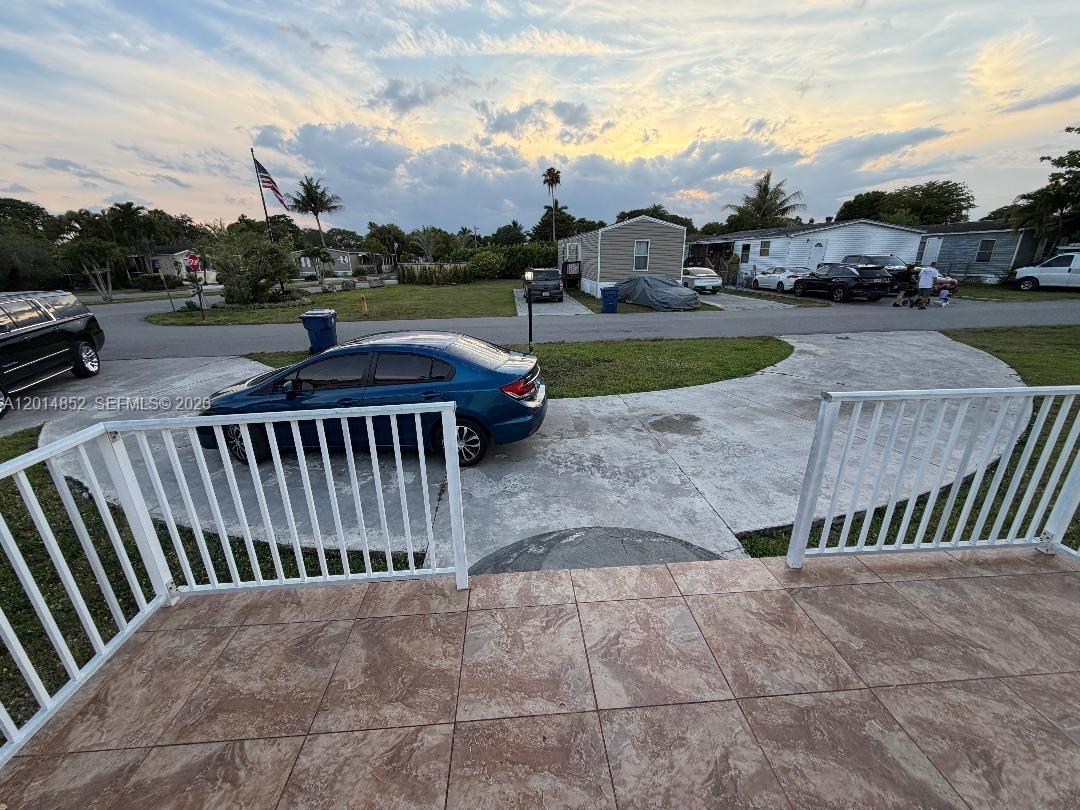 A view from a tiled porch overlooking a driveway, a blue sedan, and neighborhood homes — 19800 SW 180th Ave unit 105, Miami FL 33187, MIAMI, FL