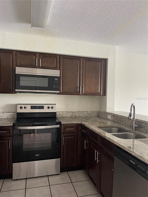 A kitchen features dark wood cabinets, granite countertops, and stainless steel appliances — 13815 FAIRWAY ISLAND DRIVE UNIT 1323, ORLANDO, FL