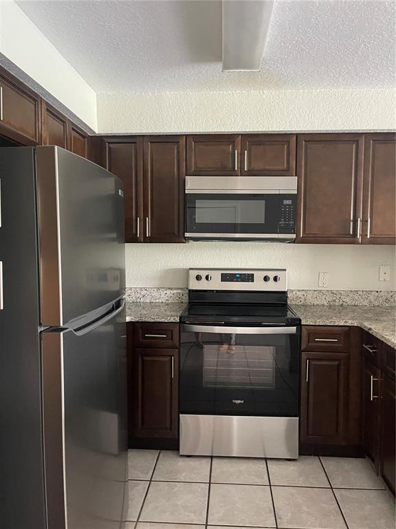 A kitchen features dark wood cabinets, stainless steel appliances, and granite countertops — 13815 FAIRWAY ISLAND DRIVE UNIT 1323, ORLANDO, FL