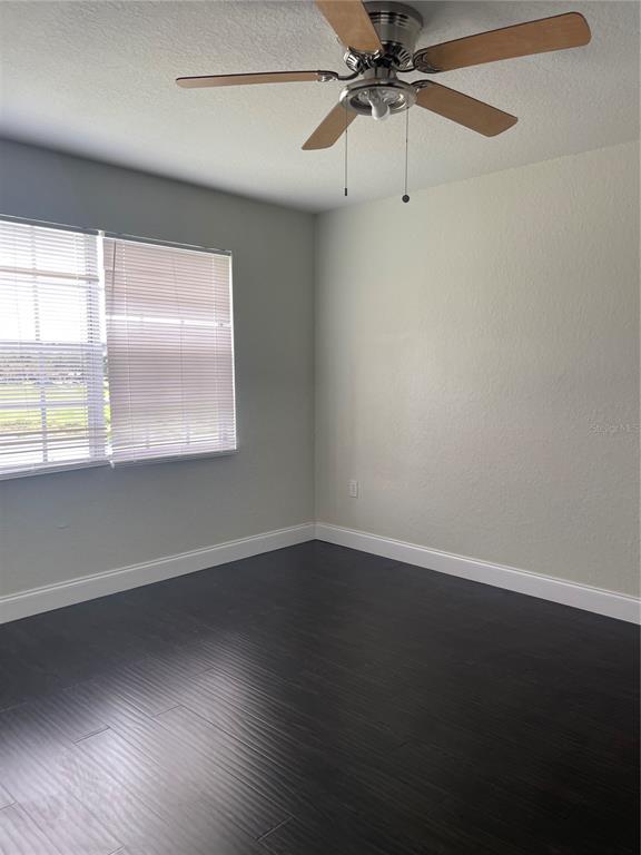 An empty room features dark wood-look flooring, light-colored walls, a ceiling fan, and a window — 13815 FAIRWAY ISLAND DRIVE UNIT 1323, ORLANDO, FL