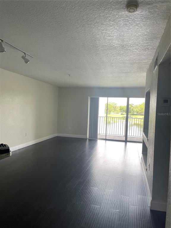 An empty living room features dark wood-look flooring, track lighting, and a sliding glass door — 13815 FAIRWAY ISLAND DRIVE UNIT 1323, ORLANDO, FL