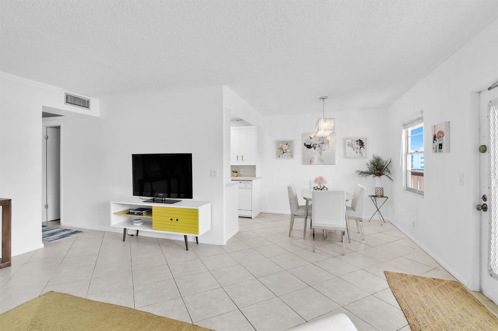 A bright living and dining area features white walls, tile flooring, and a yellow media console — 2043 Cornwall C # 2043, Boca Raton FL 33434, BOCA RATON, FL