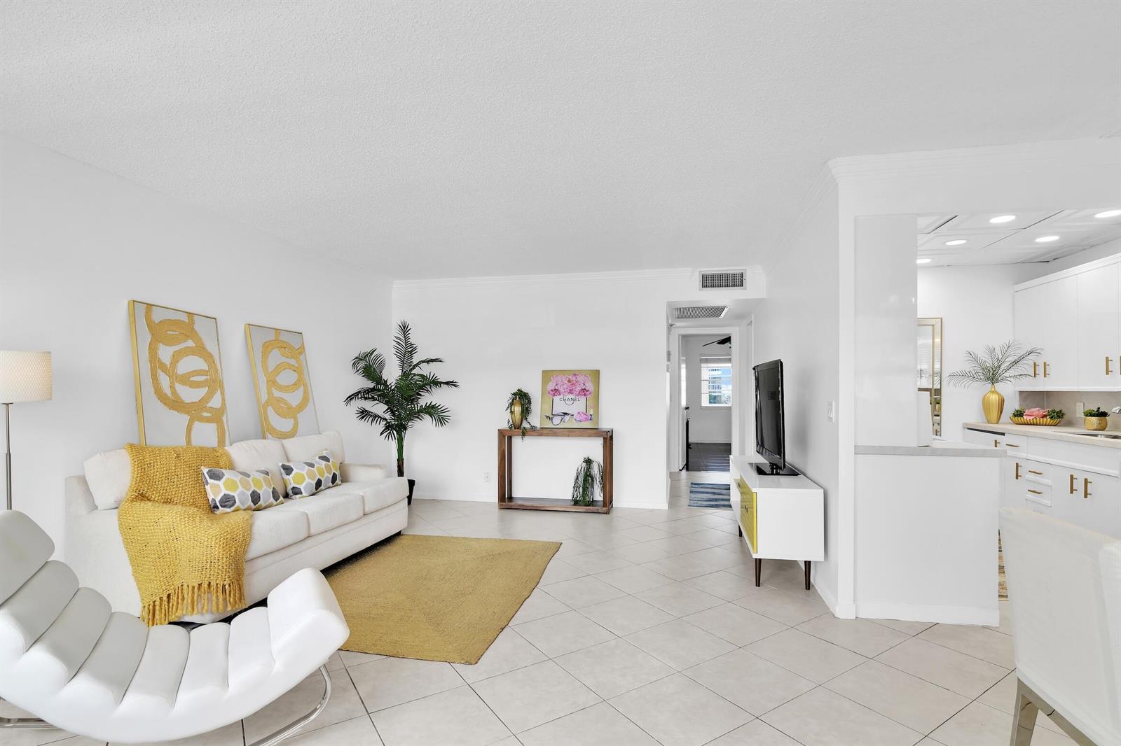 A bright living room features white walls, tile flooring, a white sofa, and yellow accents — 2043 Cornwall C # 2043, Boca Raton FL 33434, BOCA RATON, FL