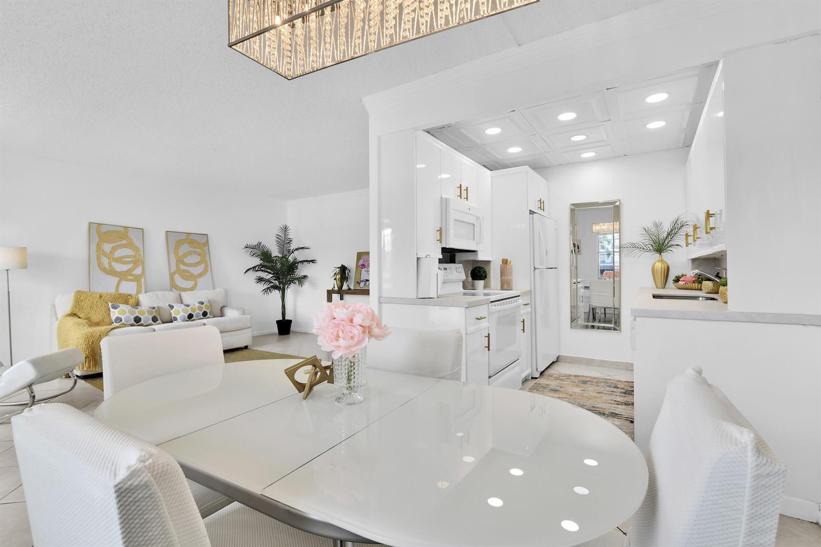 A bright, open-concept dining area and kitchen featuring white cabinetry, glossy surfaces, and modern lighting — 2043 Cornwall C # 2043, Boca Raton FL 33434, BOCA RATON, FL