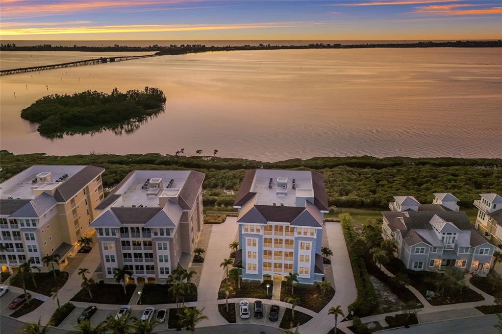 An aerial view shows three multi-story residential buildings situated along a waterfront at sunset — 376 ARUBA CIRCLE UNIT 203, BRADENTON, FL