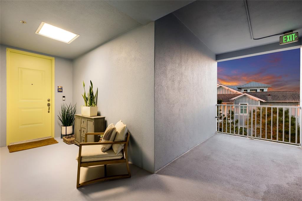 A bright yellow apartment door opens onto a covered balcony with a chair and plants — 376 ARUBA CIRCLE UNIT 203, BRADENTON, FL