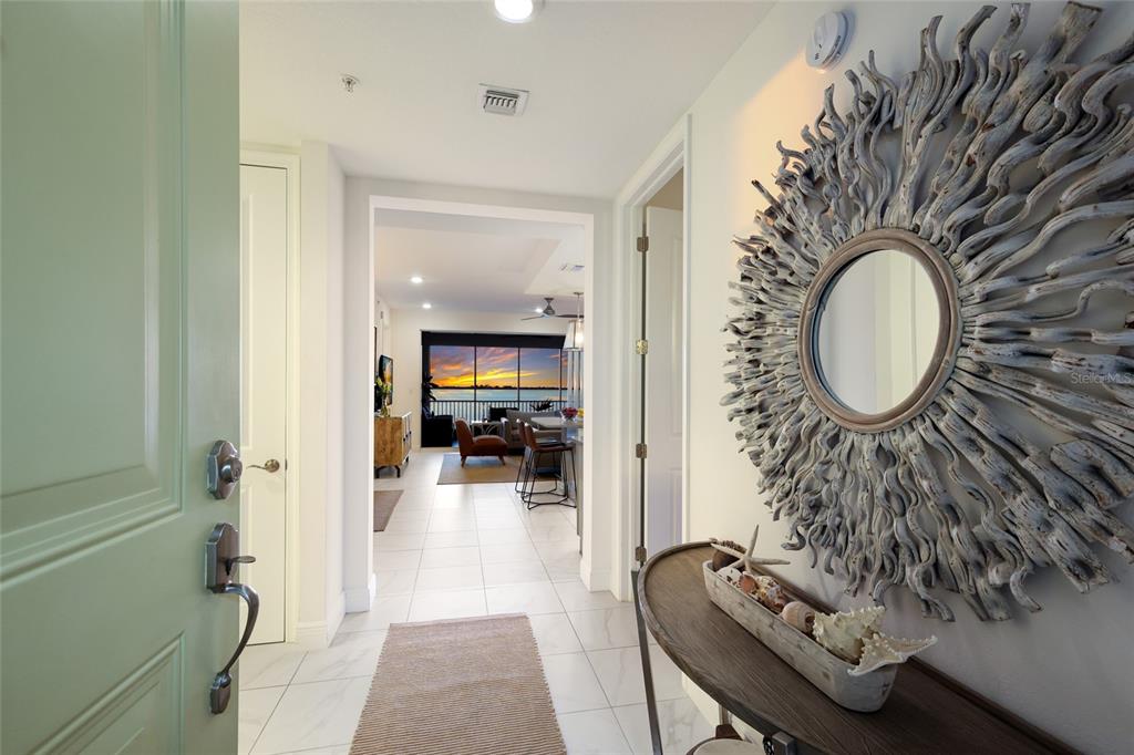 An entryway with a driftwood mirror and console table leads to a living area with water views — 376 ARUBA CIRCLE UNIT 203, BRADENTON, FL