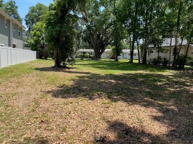 A grassy, tree-filled vacant lot sits between a white fence and a residential building — 726 CORDOVA DRIVE, ORLANDO, FL