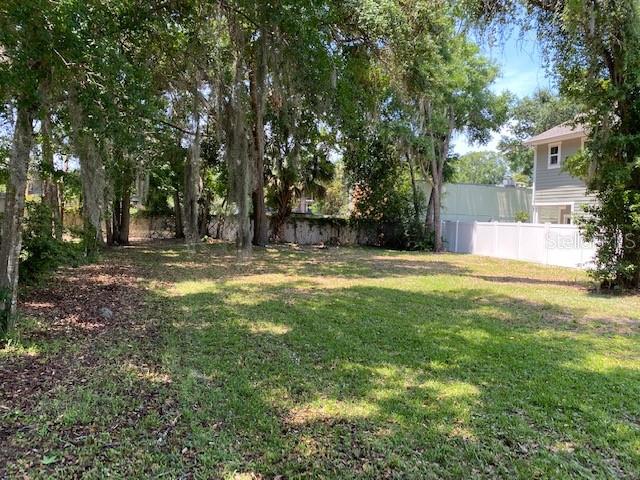 A grassy, tree-filled vacant lot sits next to a two-story house with a white fence — 726 CORDOVA DRIVE, ORLANDO, FL