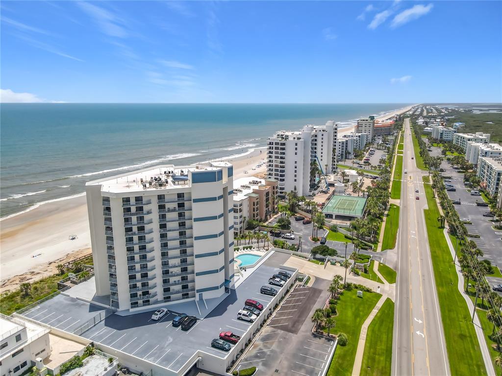 An aerial view shows a tall beachfront condominium building next to a coastal highway — 5207 S ATLANTIC AVENUE UNIT 422, NEW SMYRNA BEACH, FL