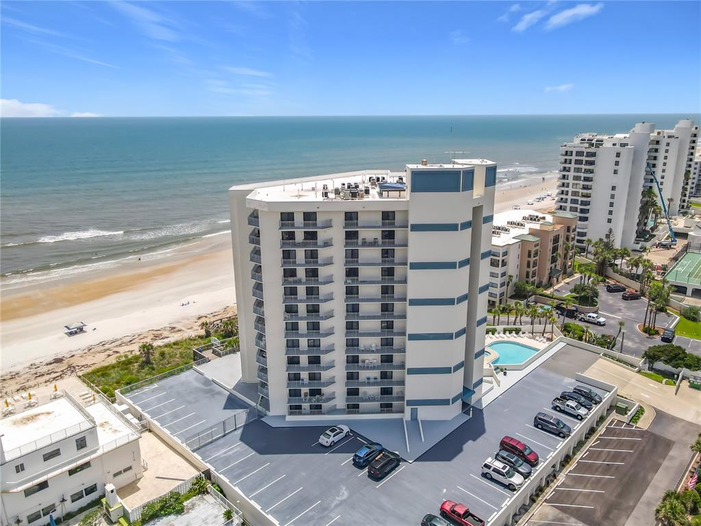 An aerial view shows a beachfront high-rise condominium building with a parking lot and ocean — 5207 S ATLANTIC AVENUE UNIT 422, NEW SMYRNA BEACH, FL