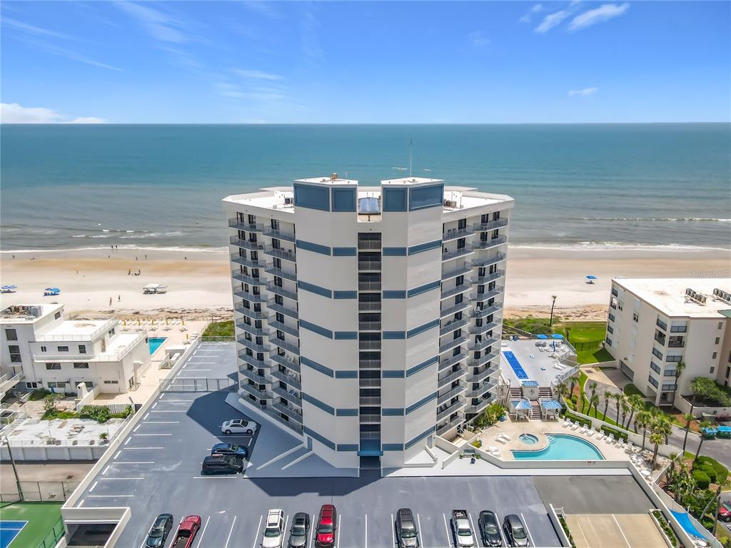 An aerial view shows a multi-story beachfront condominium building with a parking lot and pool — 5207 S ATLANTIC AVENUE UNIT 422, NEW SMYRNA BEACH, FL
