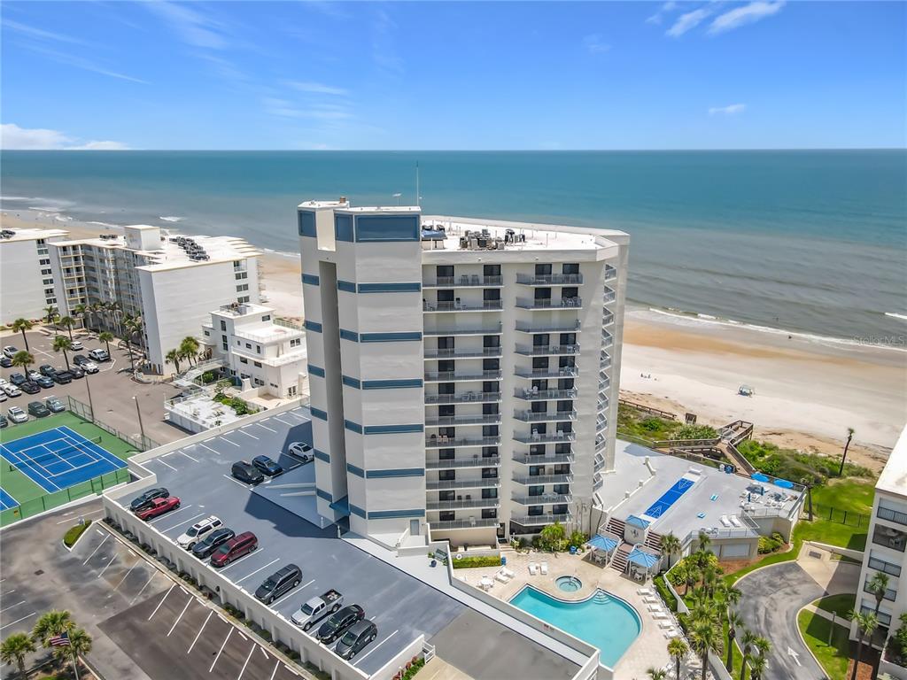 An aerial view shows a multi-story beachfront condominium building with a pool and parking lot — 5207 S ATLANTIC AVENUE UNIT 422, NEW SMYRNA BEACH, FL