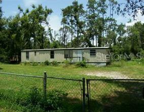 A single-story manufactured home sits on a grassy lot surrounded by mature trees — 5101 N KALIGA DRIVE, ST CLOUD, FL