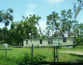 A mobile home with white siding and lattice skirting sits in a grassy, wooded lot — 5101 N KALIGA DRIVE, ST CLOUD, FL