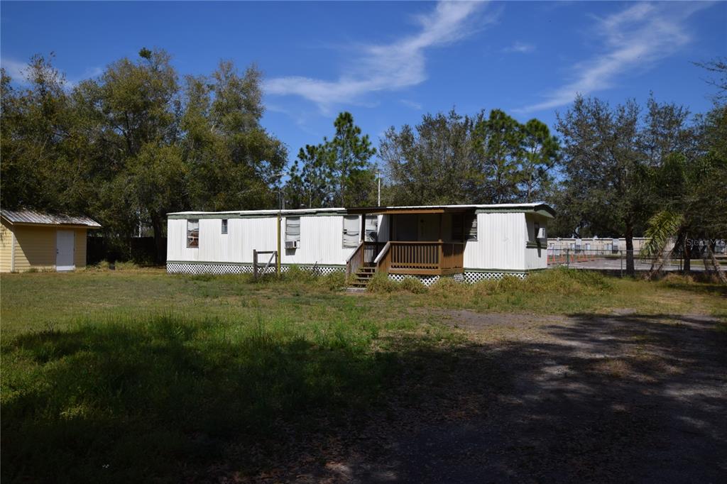 A side view of a mobile home with a small wooden deck and overgrown grass — 5101 N KALIGA DRIVE, ST CLOUD, FL