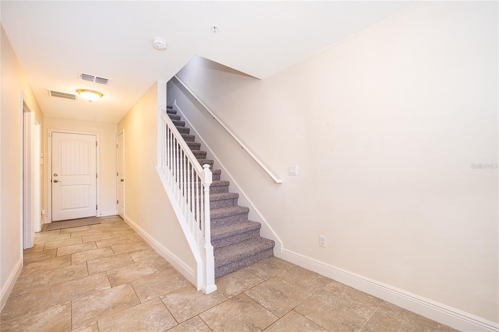 A carpeted staircase with a white railing sits in a tiled entryway with beige walls — 10061 TOWN LAKE DRIVE, ORLANDO, FL