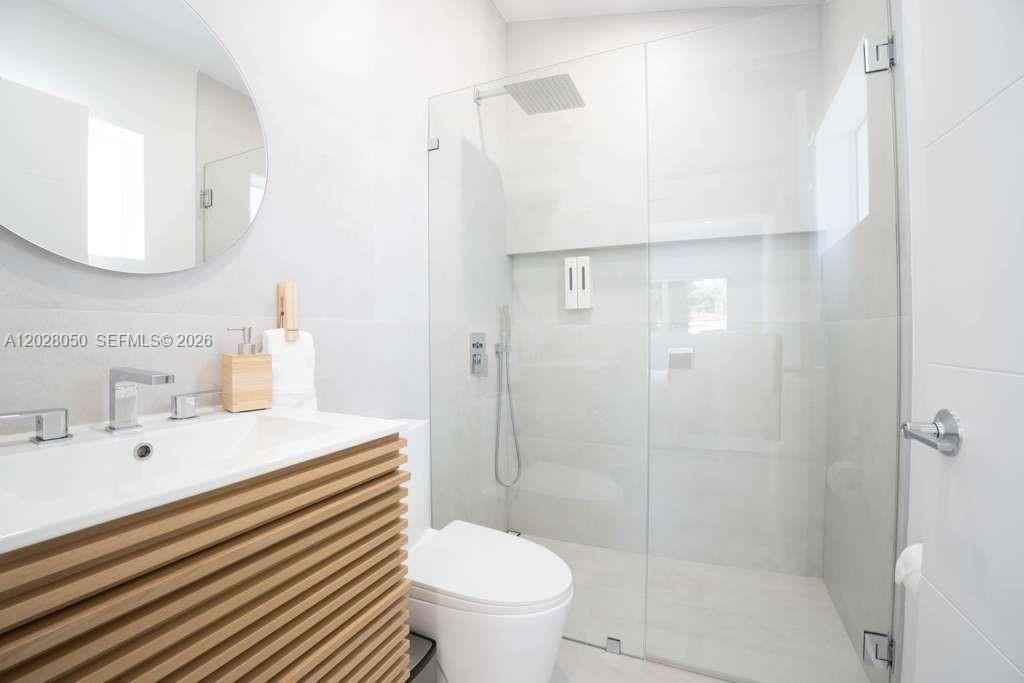 A modern bathroom features a wood-slatted vanity, a round mirror, and a glass-enclosed walk-in shower — 13800 NE 1st Ave, Miami FL 33161, MIAMI, FL