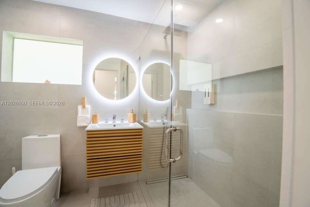 A modern bathroom features a floating wood vanity, a circular backlit mirror, and a glass-enclosed shower — 13800 NE 1st Ave, Miami FL 33161, MIAMI, FL