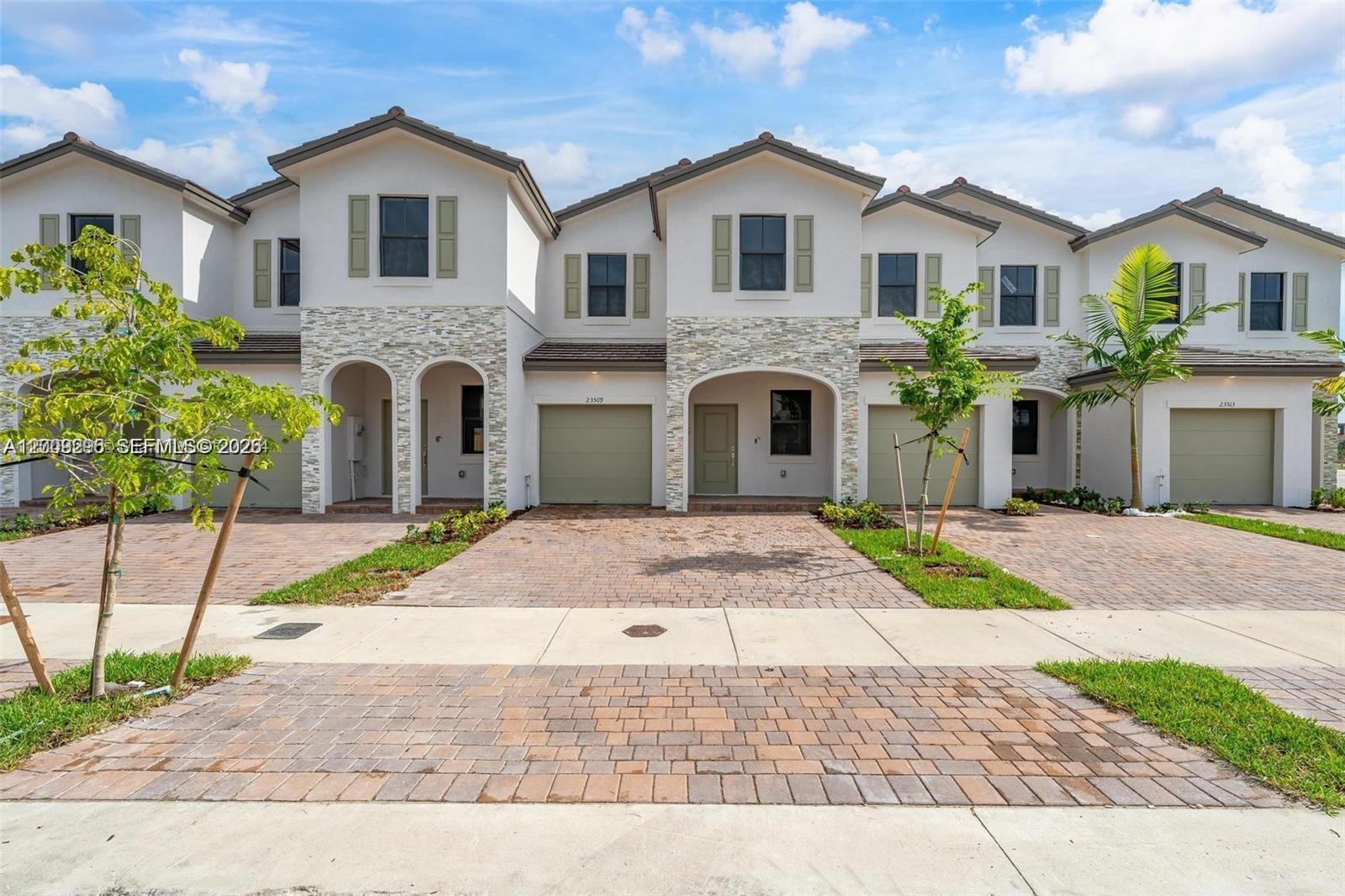 A row of multi-story townhouses features stucco facades, stone accents, and paved driveways — 23509 SW 129th Path, Homestead FL 33032, HOMESTEAD, FL