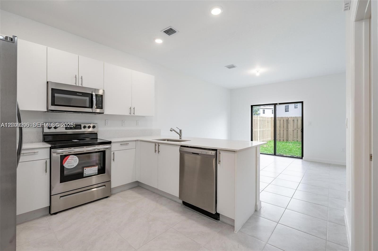 A modern kitchen features white cabinets, stainless steel appliances, and a sliding glass door — 23509 SW 129th Path, Homestead FL 33032, HOMESTEAD, FL
