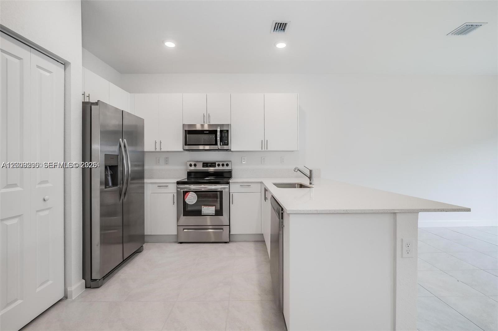 A modern kitchen features white cabinets, stainless steel appliances, and a white quartz countertop island — 23509 SW 129th Path, Homestead FL 33032, HOMESTEAD, FL