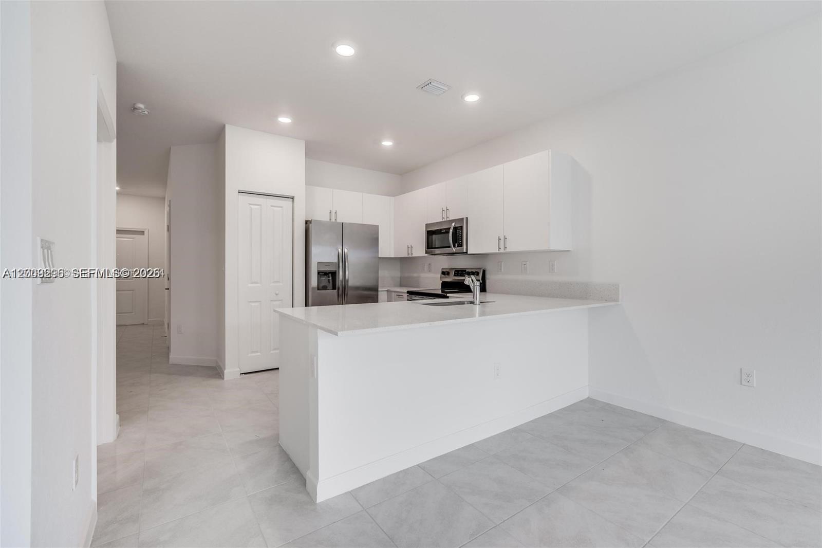 This modern kitchen features white cabinetry, stainless steel appliances, and a quartz countertop island — 23509 SW 129th Path, Homestead FL 33032, HOMESTEAD, FL