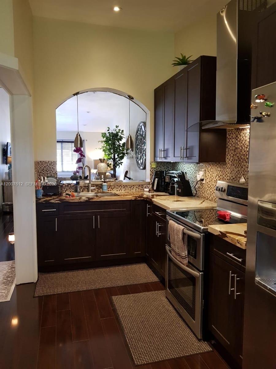 A kitchen features dark wood cabinets, stainless steel appliances, and a mosaic tile backsplash — 930 NE 33rd Ter # 202, Homestead FL 33033, HOMESTEAD, FL