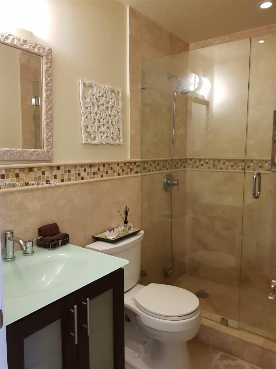 A bathroom features a glass-enclosed shower, a vanity with a glass sink, and beige tiling — 930 NE 33rd Ter # 202, Homestead FL 33033, HOMESTEAD, FL